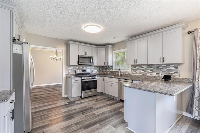 48 Savanna Ct, Powder Springs, GA 30127 - kitchen with stainless steel appliances, a peninsula, a sink, dark wood-type flooring, and a chandelier