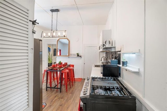 kitchen featuring decorative light fixtures, white cabinetry, sink, cooktop, and light wood-type flooring