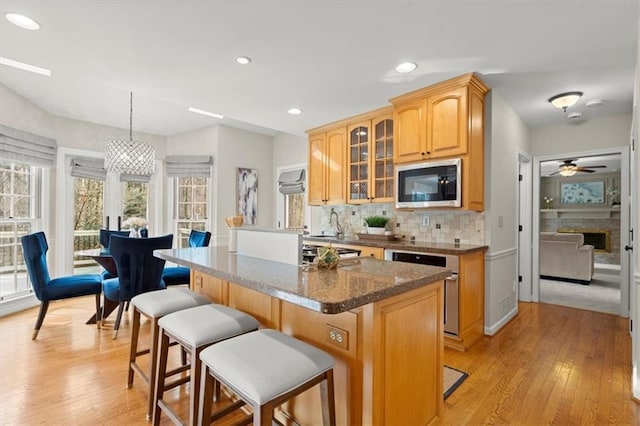 kitchen featuring pendant lighting, stainless steel microwave, dark stone countertops, a breakfast bar area, and decorative backsplash