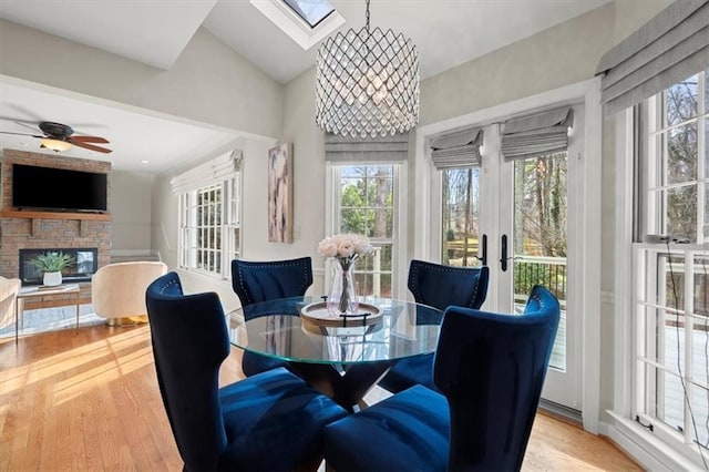 dining room with an inviting chandelier, a stone fireplace, vaulted ceiling with skylight, and light hardwood / wood-style flooring