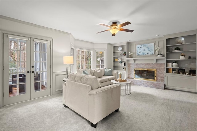 living room with ceiling fan, ornamental molding, light carpet, a brick fireplace, and french doors