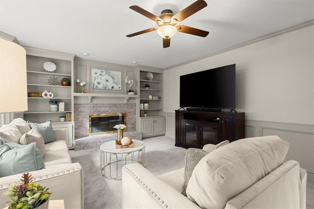 living room with a fireplace, ornamental molding, light colored carpet, ceiling fan, and built in shelves