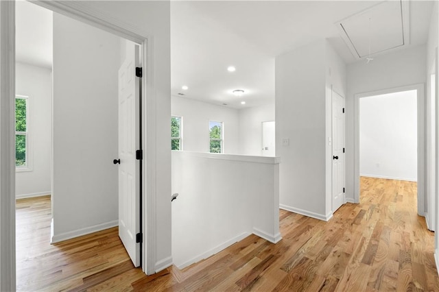 corridor with an upstairs landing, light wood finished floors, attic access, and baseboards