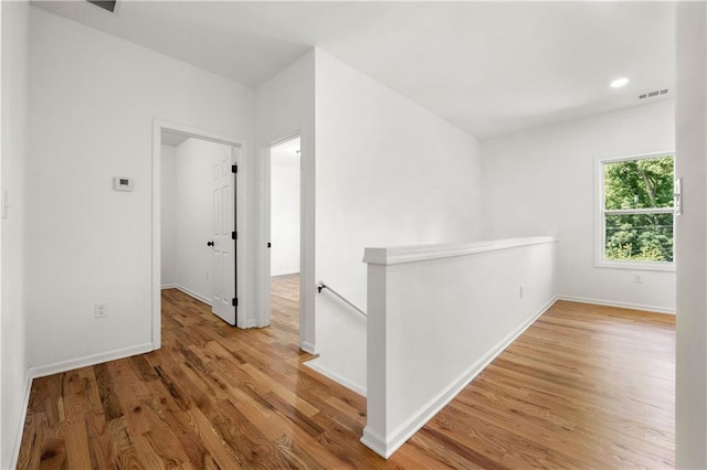 hallway with wood finished floors, an upstairs landing, visible vents, and baseboards