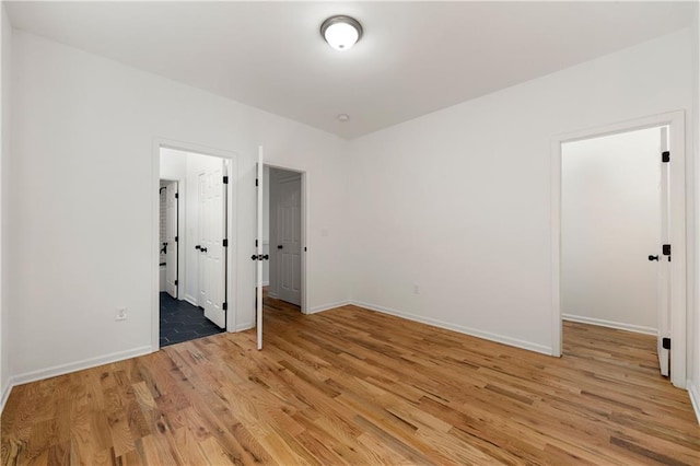 unfurnished bedroom with light wood-style flooring, a walk in closet, and baseboards