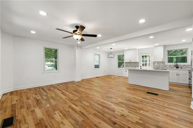 unfurnished living room with light wood-type flooring, visible vents, a sink, recessed lighting, and baseboards