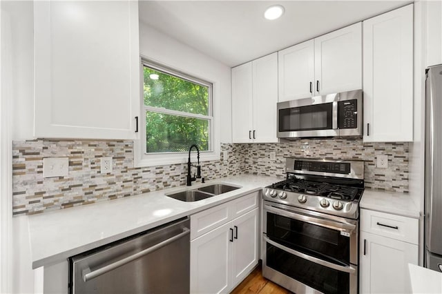 kitchen with a sink, decorative backsplash, light countertops, stainless steel appliances, and white cabinetry