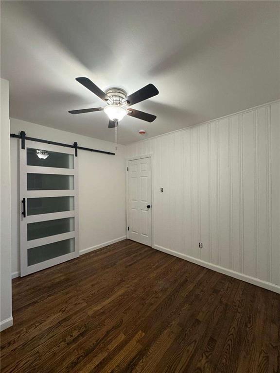 spare room featuring a ceiling fan, wood finished floors, baseboards, and a barn door