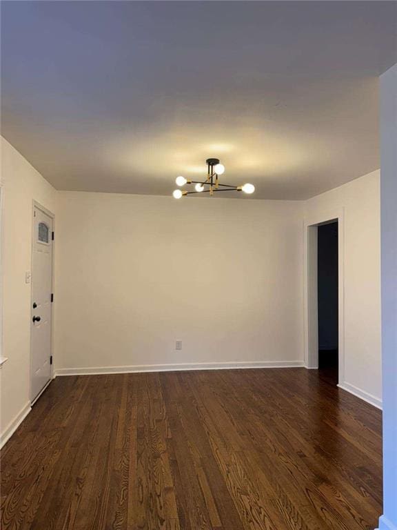 unfurnished room featuring dark wood-style floors, a chandelier, and baseboards