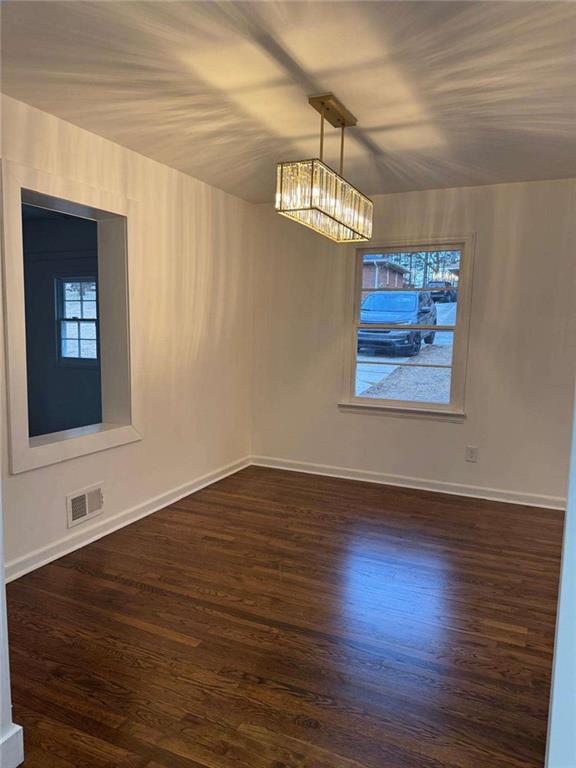 unfurnished room with baseboards, visible vents, a chandelier, and dark wood-style flooring