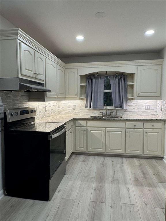 kitchen with light wood finished floors, electric stove, backsplash, under cabinet range hood, and a sink