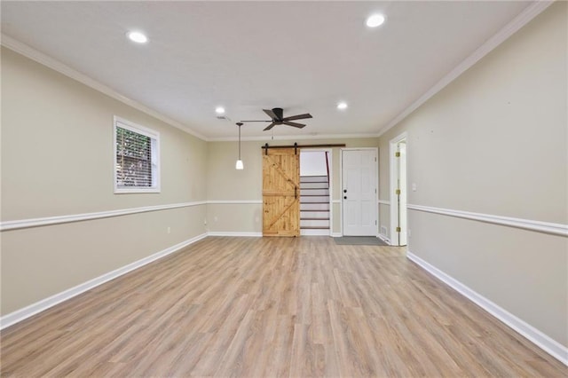 empty room featuring a barn door, crown molding, ceiling fan, and light hardwood / wood-style floors