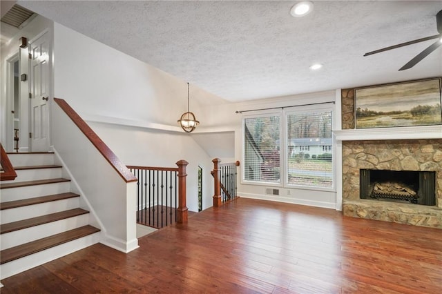 living room with hardwood / wood-style floors, ceiling fan, a stone fireplace, and a textured ceiling