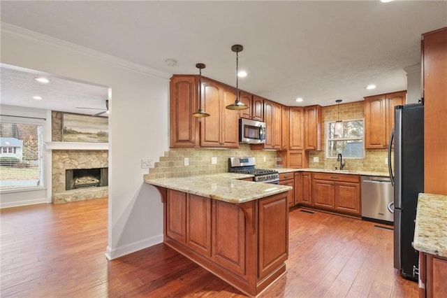 kitchen featuring stainless steel appliances, a stone fireplace, kitchen peninsula, crown molding, and pendant lighting