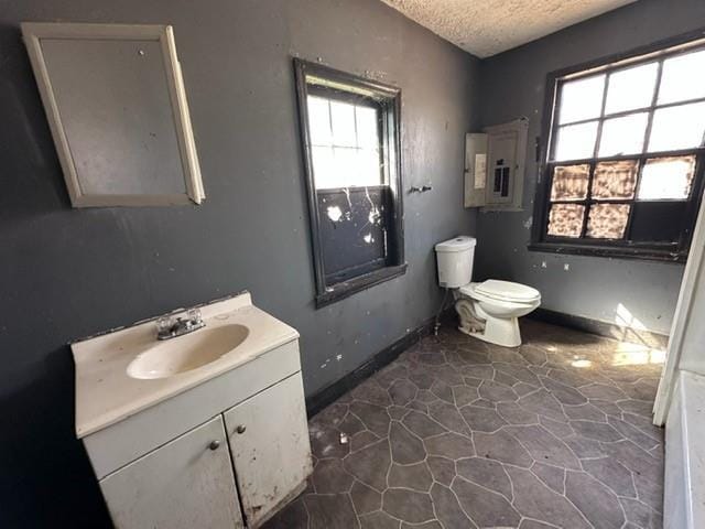 bathroom with toilet, electric panel, a textured ceiling, baseboards, and vanity