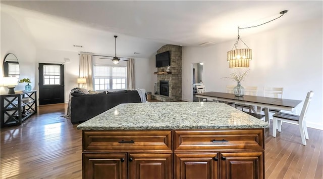 kitchen with dark hardwood / wood-style floors, a fireplace, hanging light fixtures, a center island, and light stone countertops