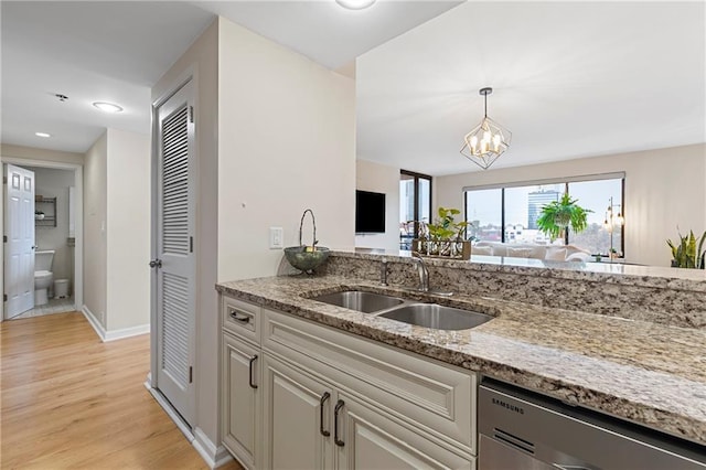 kitchen with sink, light hardwood / wood-style flooring, light stone counters, stainless steel dishwasher, and a chandelier