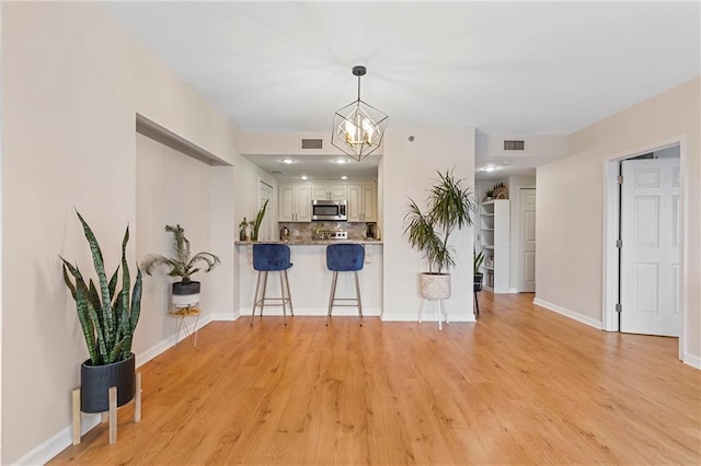 kitchen with pendant lighting, light hardwood / wood-style flooring, a kitchen breakfast bar, tasteful backsplash, and kitchen peninsula