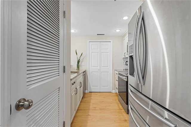 kitchen with stainless steel appliances, light hardwood / wood-style floors, and white cabinets