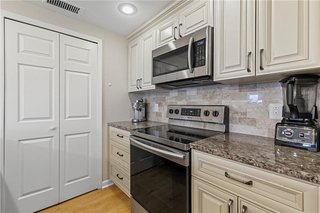 kitchen featuring tasteful backsplash, stainless steel appliances, light hardwood / wood-style flooring, and dark stone countertops