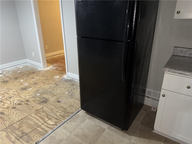 kitchen featuring freestanding refrigerator, baseboards, light stone counters, and white cabinetry