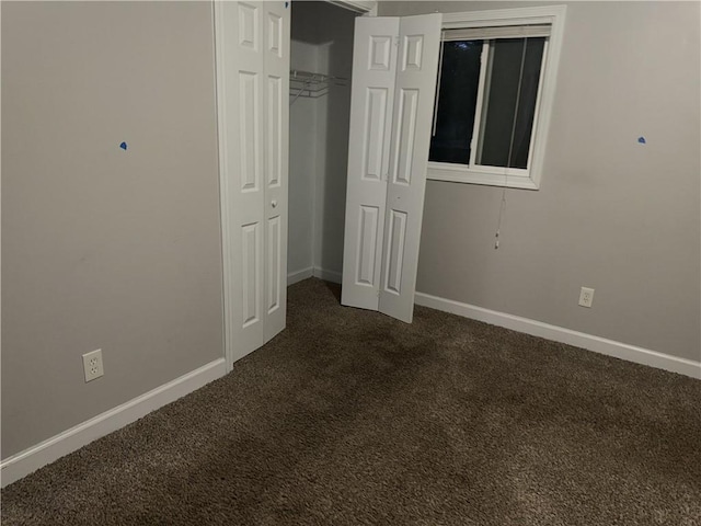 unfurnished bedroom with dark carpet, baseboards, and a closet
