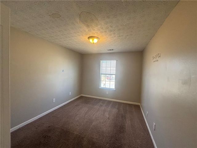 spare room featuring visible vents, a textured ceiling, baseboards, and dark colored carpet