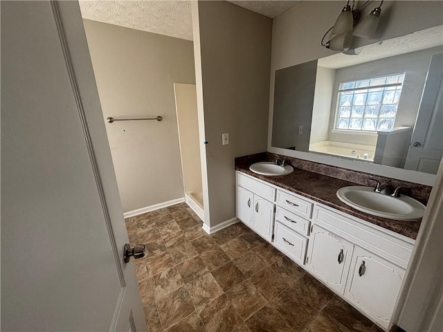 bathroom featuring a textured ceiling, a bath, baseboards, and a sink