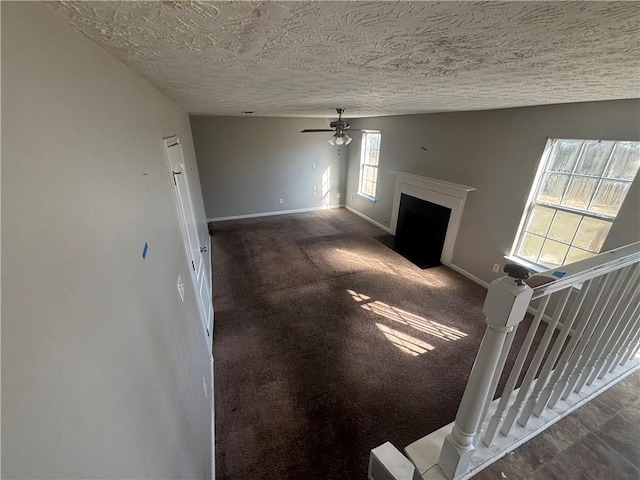 unfurnished living room featuring baseboards, carpet, ceiling fan, a fireplace with flush hearth, and a textured ceiling