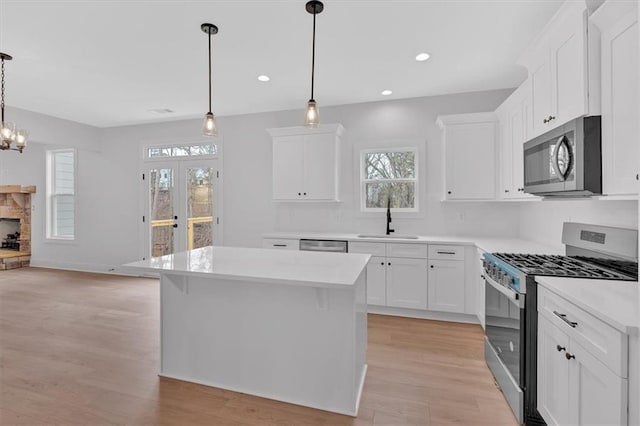 kitchen with a center island, sink, decorative light fixtures, white cabinetry, and stainless steel appliances