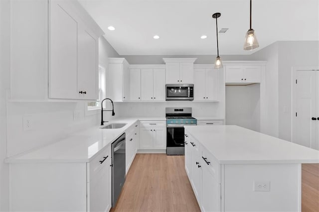 kitchen with white cabinetry, sink, stainless steel appliances, decorative light fixtures, and a kitchen island