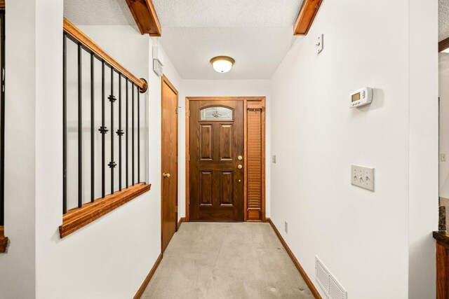 doorway to outside with a textured ceiling and light carpet