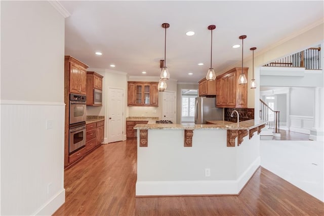 2748 Hidden Falls Dr, Buford, GA 30519 - kitchen featuring a peninsula, stainless steel appliances, brown cabinetry, ornamental molding, and a kitchen bar