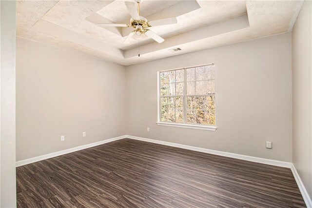 empty room featuring a raised ceiling, ceiling fan, and dark wood-type flooring