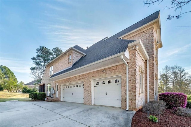 view of side of home featuring concrete driveway, an attached garage, a shingled roof, and brick siding