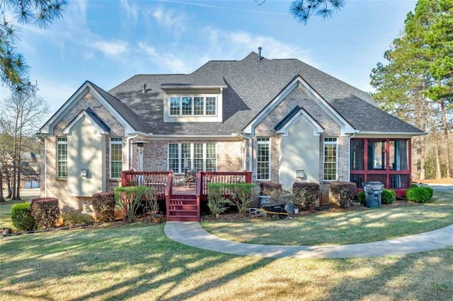 view of front of property featuring roof with shingles, a deck, a front lawn, and stone siding