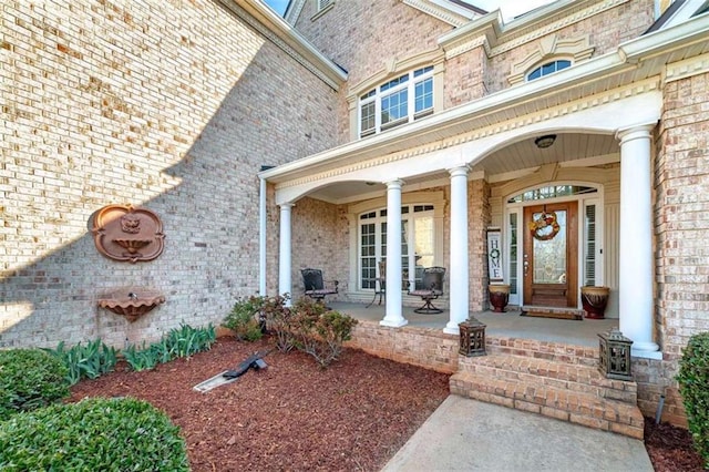view of exterior entry with brick siding and a porch