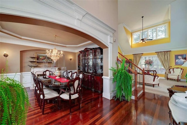 dining space featuring wood finished floors, arched walkways, stairs, a decorative wall, and a wainscoted wall