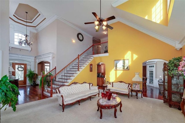 carpeted living room with a towering ceiling, arched walkways, and ceiling fan with notable chandelier