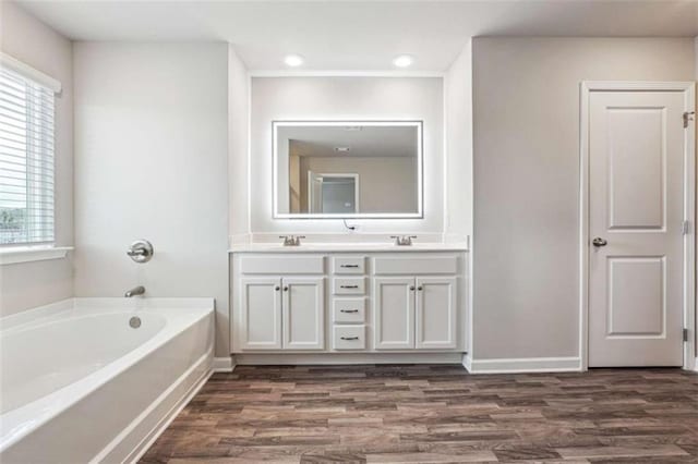 full bathroom with a sink, double vanity, wood finished floors, and a bath