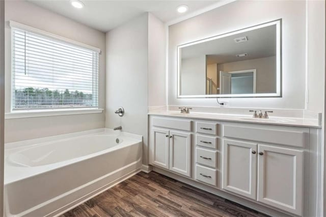 full bathroom featuring double vanity, a garden tub, a sink, and wood finished floors