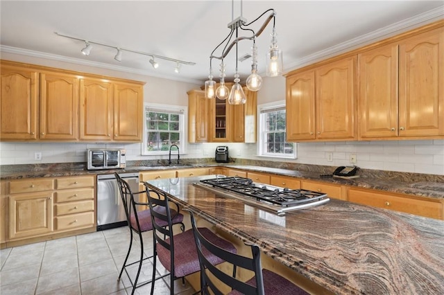 kitchen featuring dark stone counters, ornamental molding, decorative light fixtures, light tile patterned flooring, and stainless steel appliances