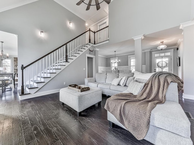 living room with decorative columns, dark wood-type flooring, crown molding, high vaulted ceiling, and a chandelier