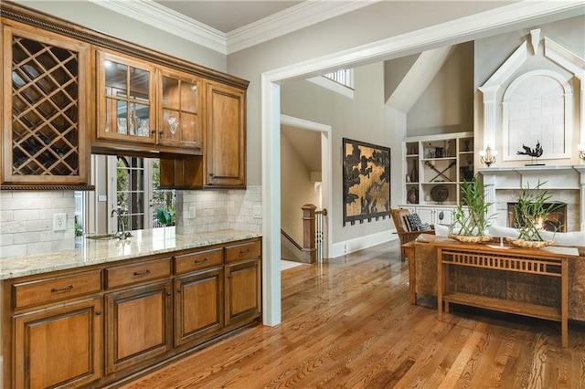 bar featuring a warm lit fireplace, baseboards, light wood-style flooring, crown molding, and a sink