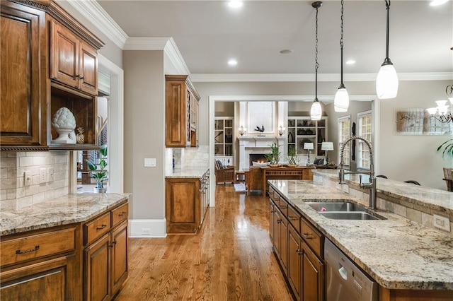 kitchen with dishwasher, open floor plan, wood finished floors, a lit fireplace, and a sink