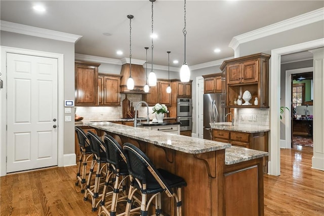 kitchen with appliances with stainless steel finishes, light wood-type flooring, brown cabinetry, and a spacious island