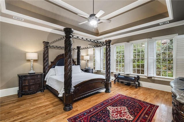 bedroom featuring wood finished floors, visible vents, baseboards, a raised ceiling, and crown molding