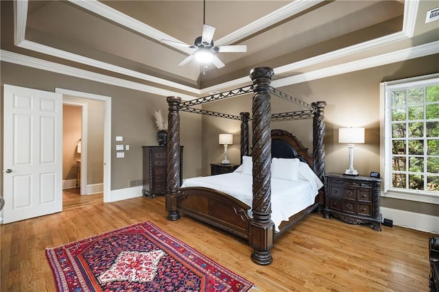 bedroom featuring a raised ceiling, crown molding, light wood-style flooring, and baseboards