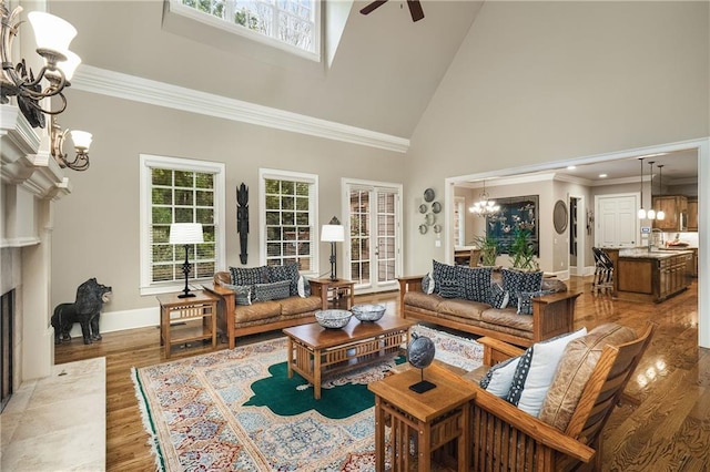 living room with high vaulted ceiling, ceiling fan with notable chandelier, a fireplace, wood finished floors, and crown molding