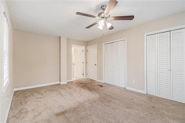 unfurnished bedroom with ceiling fan, carpet floors, a textured ceiling, and two closets